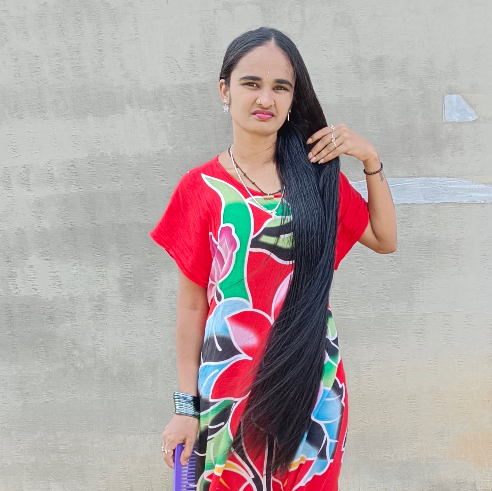 Woman in a colorful dress holding a long black hair against a plain background